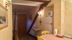 A cozy room with a wooden floor, a table with a plaid tablecloth, a yellow chair, a white refrigerator, and a small table with a lamp and a picture frame. - SUMMIT CONTINUATION (Méolans-Revel)