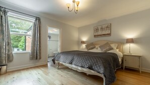 A bedroom with a large bed, a chandelier, a bedside table with a lamp, and a window with curtains.