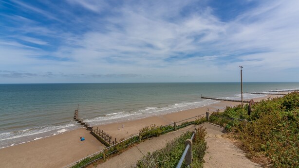 A beach with a wooden walkway leading to the shore, a sandy beach, and the ocean.