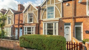 A row of terraced houses with brick facades, white-framed windows, and a well-maintained hedge in front.