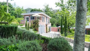 A brick house with a covered patio and a garden with various plants. - Romantic hideaway with Mountain Views (Cape Town)