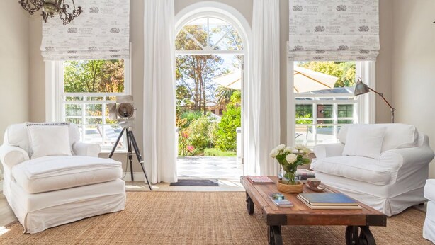 A spacious living room with two white sofas, a wooden coffee table, and a large window with a view of greenery. - Romantic hideaway with Mountain Views (Cape Town)