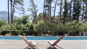 Two wooden lounge chairs by a swimming pool with a backdrop of tall trees and a mountain. - Romantic hideaway with Mountain Views (Cape Town)