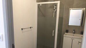 Une salle de bain moderne avec une douche à parois de verre, des toilettes et un lavabo surmonté d’un miroir.