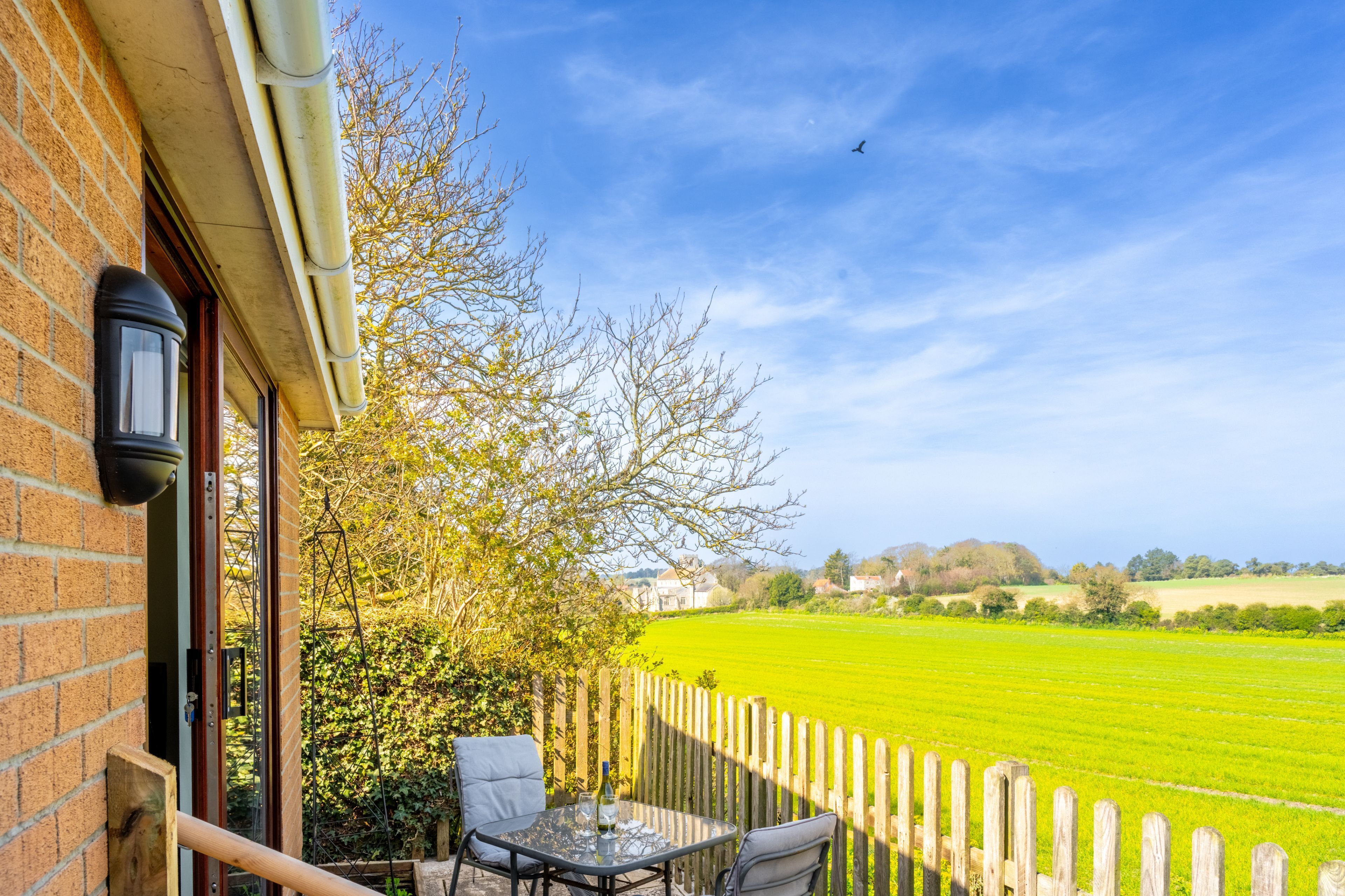 A patio with a table and chairs, a brick wall, a wooden fence, and a view of a green field.