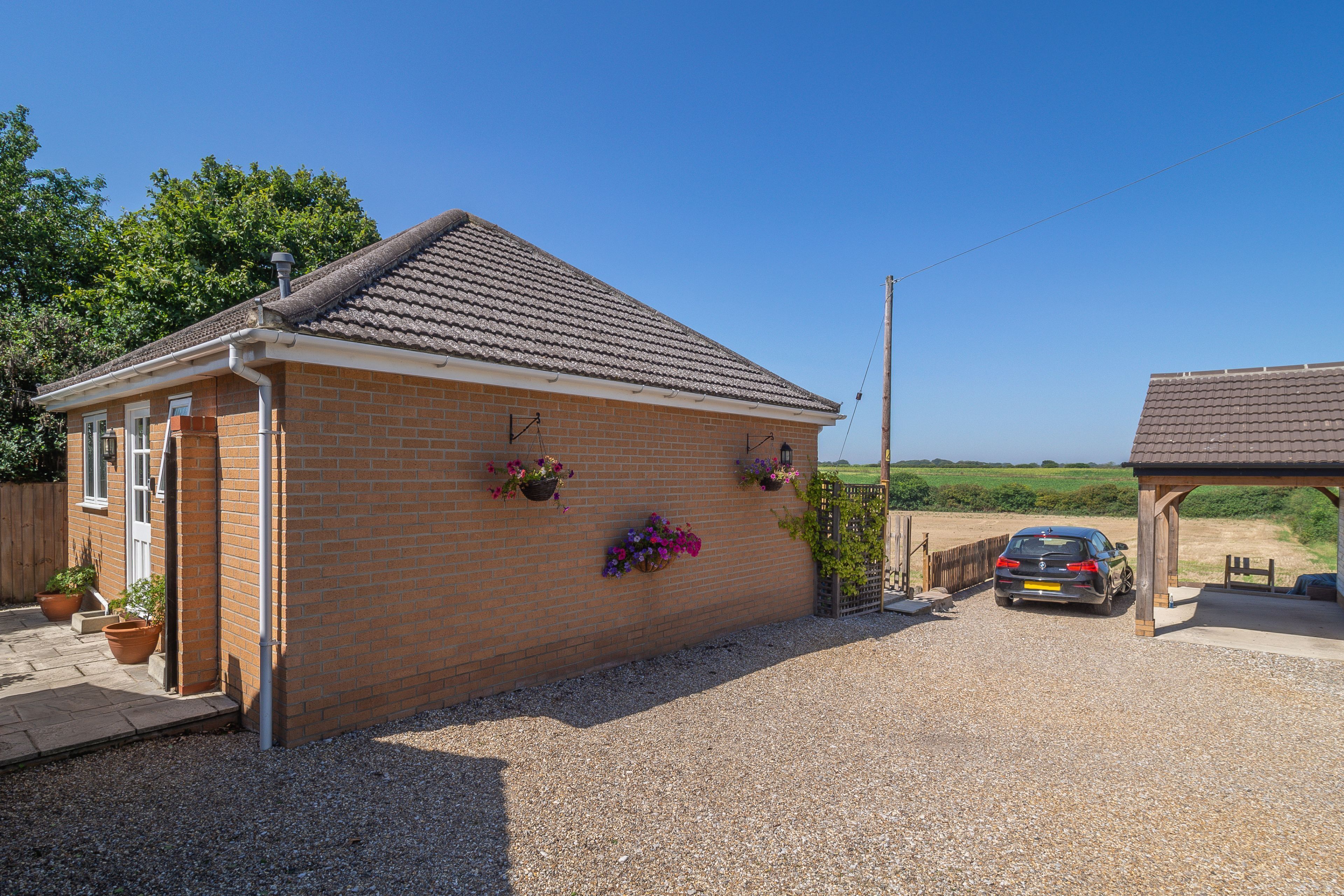 A small brick building with a tiled roof, a car parked in front, and a gravel driveway.