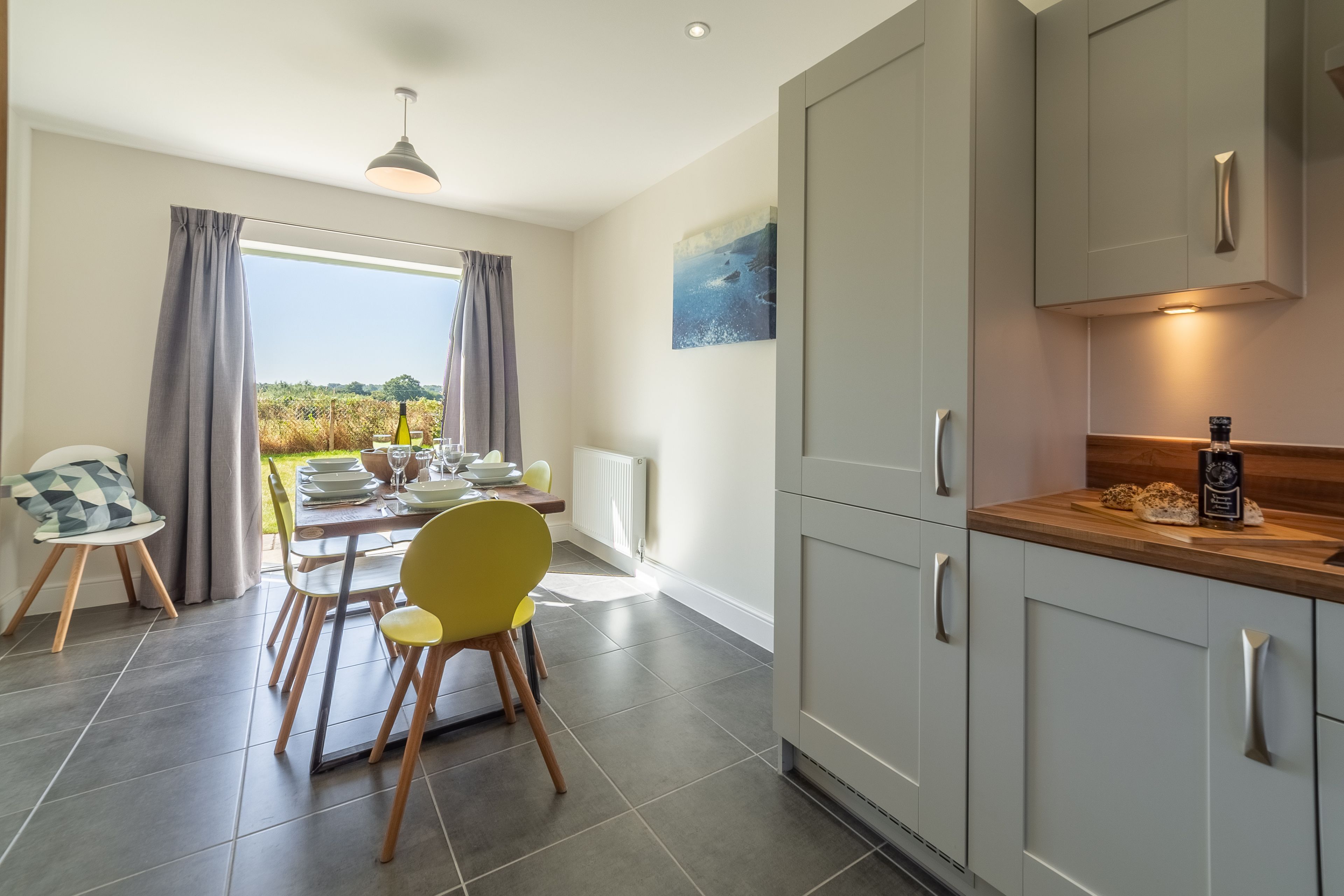 A modern kitchen with grey cabinets, a wooden countertop, and a dining area with a table and chairs.