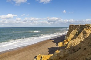 A coastal beach with a cliff and ocean waves. - Samphire House, Bodham, Norfolk (Bodham)