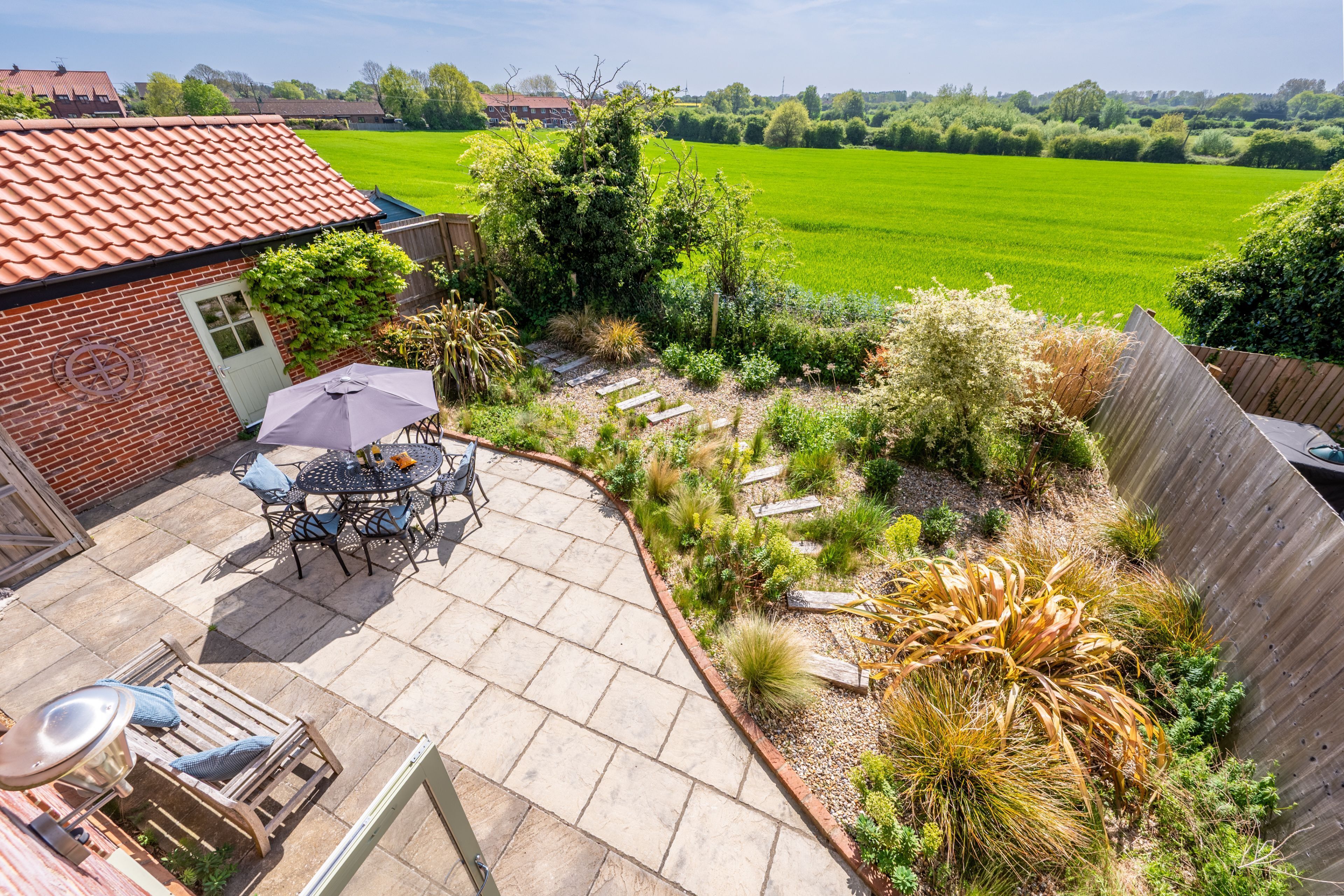 Eine Terrasse mit Tisch und Stühlen, umgeben von einem Garten mit verschiedenen Pflanzen und einem Holzzaun.