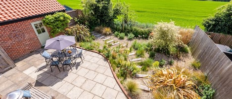 Eine Terrasse mit Tisch und Stühlen, umgeben von einem Garten mit verschiedenen Pflanzen und einem Holzzaun.