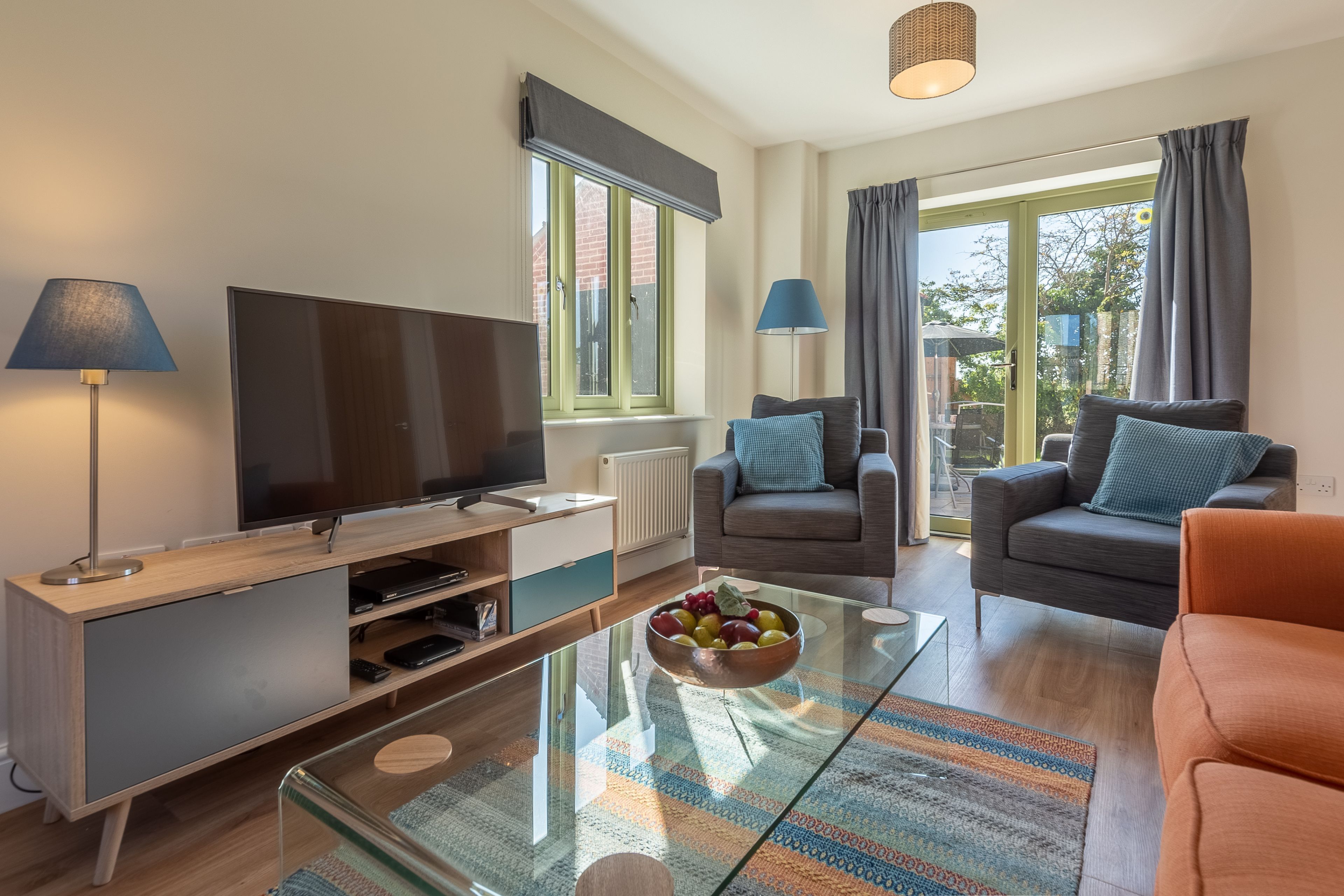 A modern living room with a flat-screen TV, two sofas, a coffee table with fruit, and a glass-top table.