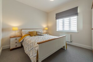 Une chambre à coucher avec un lit, des lampes de chevet, une fenêtre avec des stores et un radiateur.