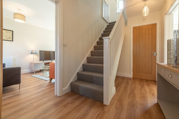 A staircase leading to a wooden door, a living area with a TV, a lamp, and a sofa. - Samphire House, Bodham, Norfolk (Bodham)