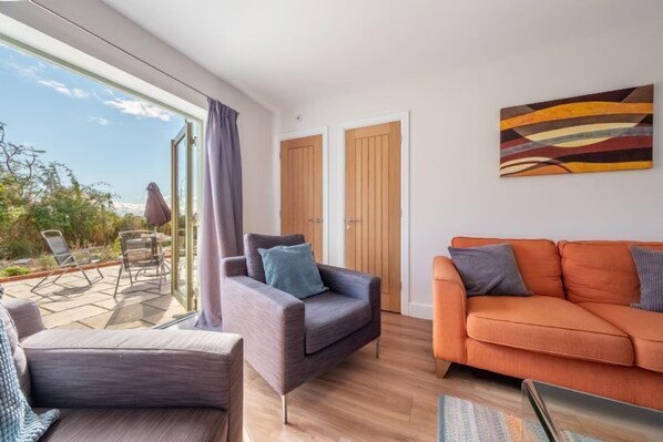 Un salon moderne avec un canapé, un fauteuil et une porte vitrée donnant sur une terrasse extérieure.
