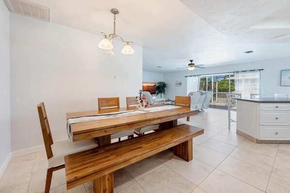 A spacious dining area with a wooden table and benches, a ceiling fan, and a view of the outdoors.