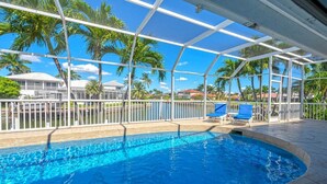 A swimming pool with a clear view of palm trees and a building in the background. - Island Oasis-Waterfront Pool home! 10 min walk to the beach! (Marco Island)
