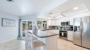 A modern kitchen with white cabinets, stainless steel appliances, and a bar area with stools. - Island Oasis-Waterfront Pool home! 10 min walk to the beach! (Marco Island)