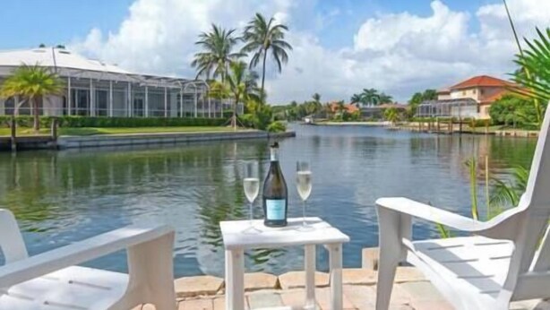 A riverside view with a table set for two, a bottle of wine, and a glass on the table. - Island Oasis-Waterfront Pool home! 10 min walk to the beach! (Marco Island)