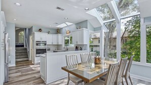 A modern kitchen with white cabinetry, a central island, and a dining area with a glass table. - Spectacular home located on the Robert Trent Jones Golf Course (Hilton Head)