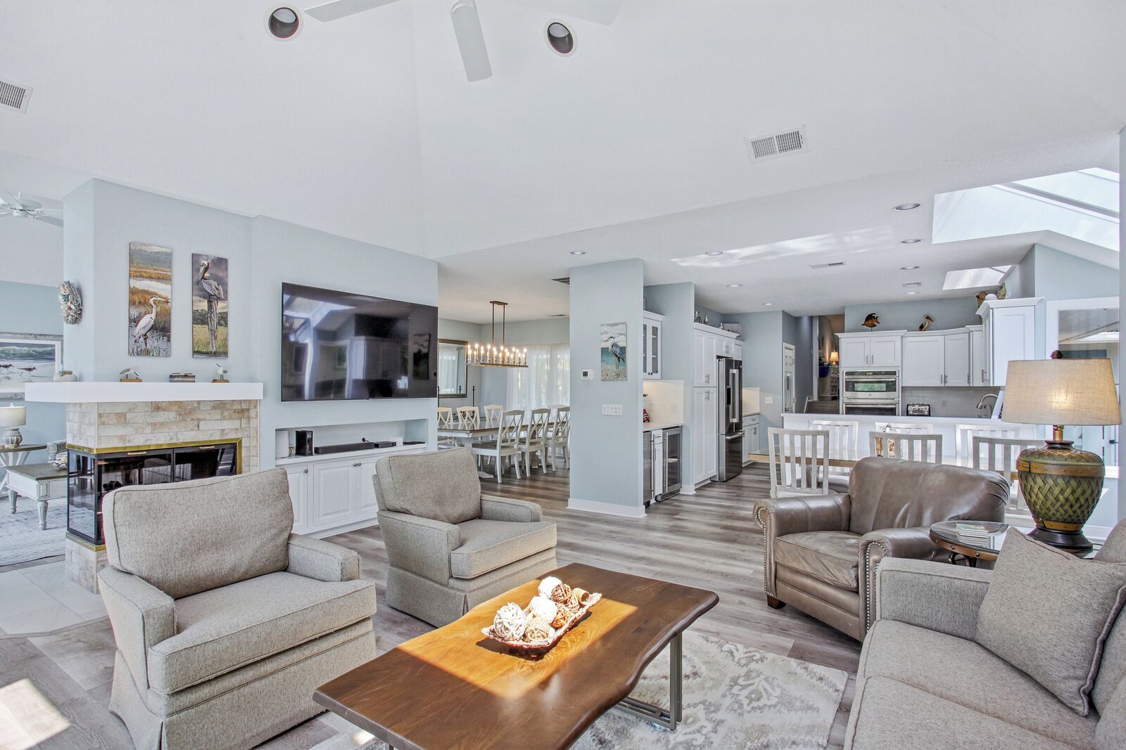 A spacious living room with a fireplace, comfortable seating, a large TV, and a view into the kitchen area.