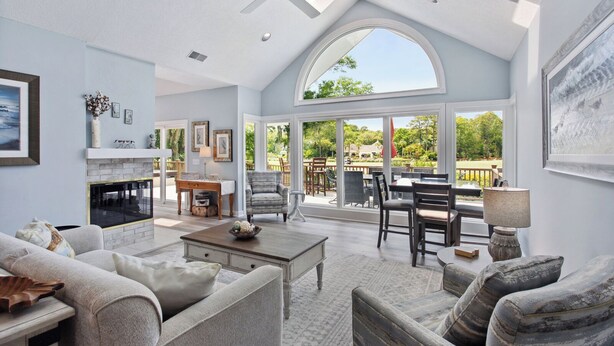 A spacious living room with a fireplace, comfortable seating, and large windows offering a view of the outdoors. - Spectacular home located on the Robert Trent Jones Golf Course (Hilton Head)