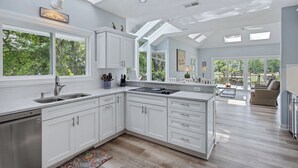 A modern kitchen with white cabinetry, a large island, and a dining area with a view of the outdoors. - Spectacular home located on the Robert Trent Jones Golf Course (Hilton Head)