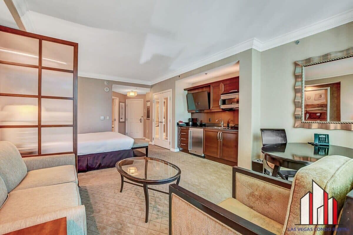 Een hotelkamer met een bed, een slaapbank, een tafeltje, een kitchenette en een spiegel.