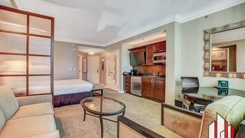 Een hotelkamer met een bed, een slaapbank, een tafeltje, een kitchenette en een spiegel.