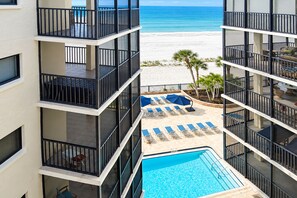 A hotel with a pool, lounge chairs, and a view of the beach.