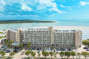 A multi-story hotel with a parking lot and a view of the beach and ocean.