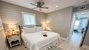 A bedroom with a bed, a nightstand, a ceiling fan, a window, and a door leading to another room. - Beachfront-Top floor, corner. Waterfront views! Smart TVs and WiFi. Sleeps 2 (Tybee Island)