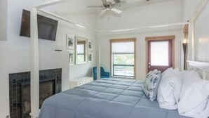 A bedroom with a bed, a fireplace, a ceiling fan, a window, and a door.
