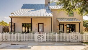 A two-story building with a white picket fence, a covered porch, and a metal roof.