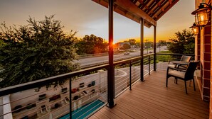 A wooden deck with a view of a road and trees, a railing, and a table with chairs.