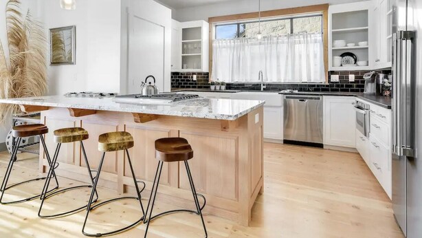A modern kitchen with a large island, bar stools, stainless steel appliances, and a view of the outdoors.