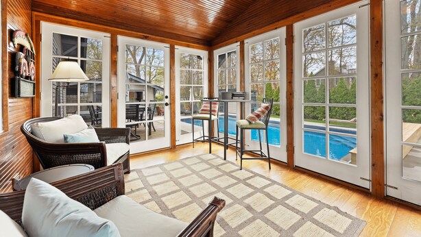 Une pièce spacieuse avec un plafond en bois, de grandes fenêtres, une piscine et du mobilier d’extérieur.