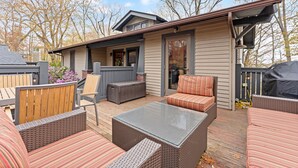 Une terrasse extérieure couverte, aménagée avec des meubles en osier, une table à plateau de verre et un barbecue.