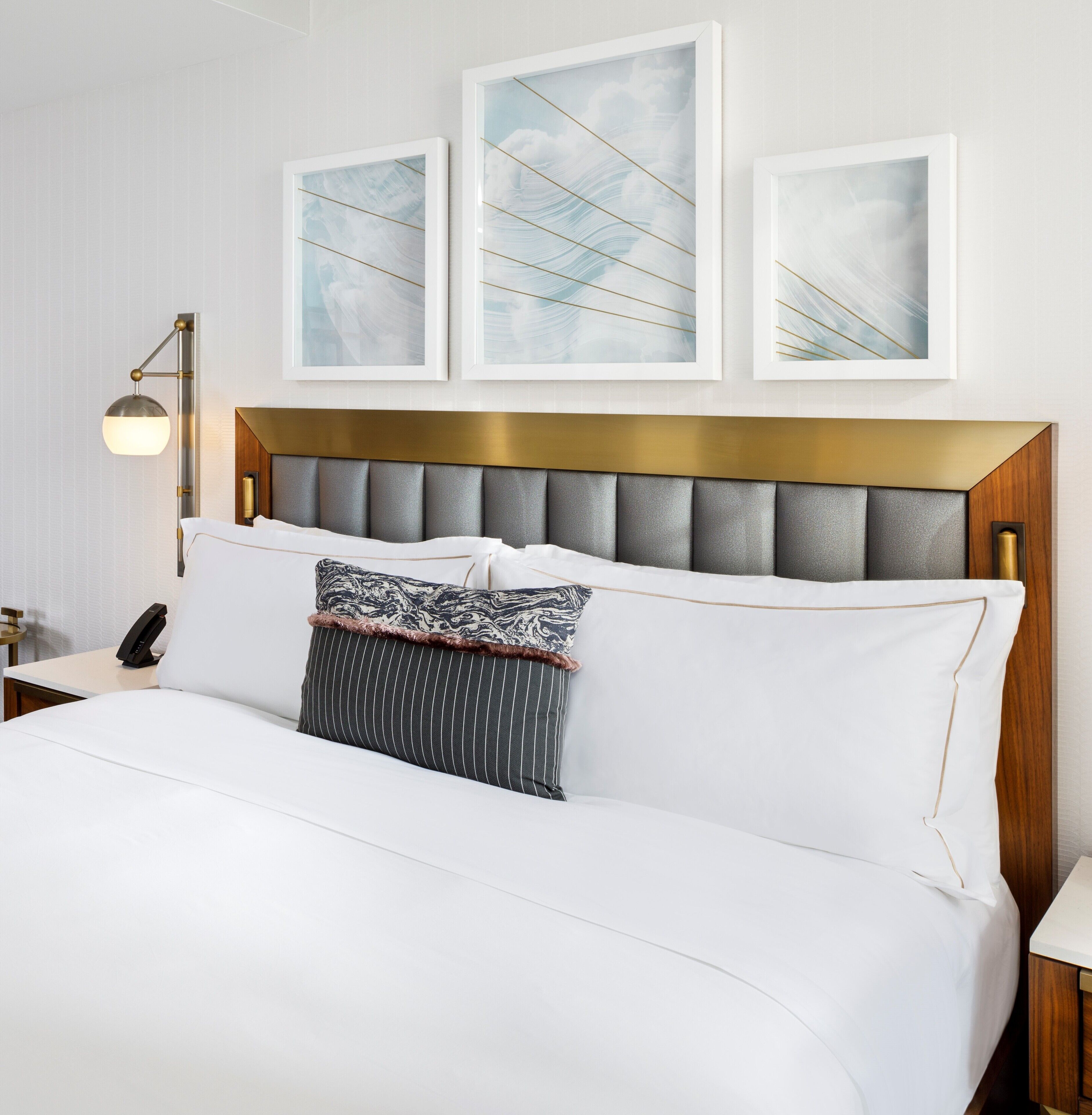 Una habitación de hotel con una cama grande, un cabecero moderno y tres obras de arte enmarcadas sobre la cama.