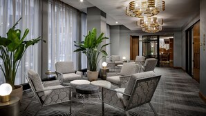 En moderne hotellobby med et siddeområde med mønstrede stole og skamler, en stor stueplante og et unikt loftslampe.
