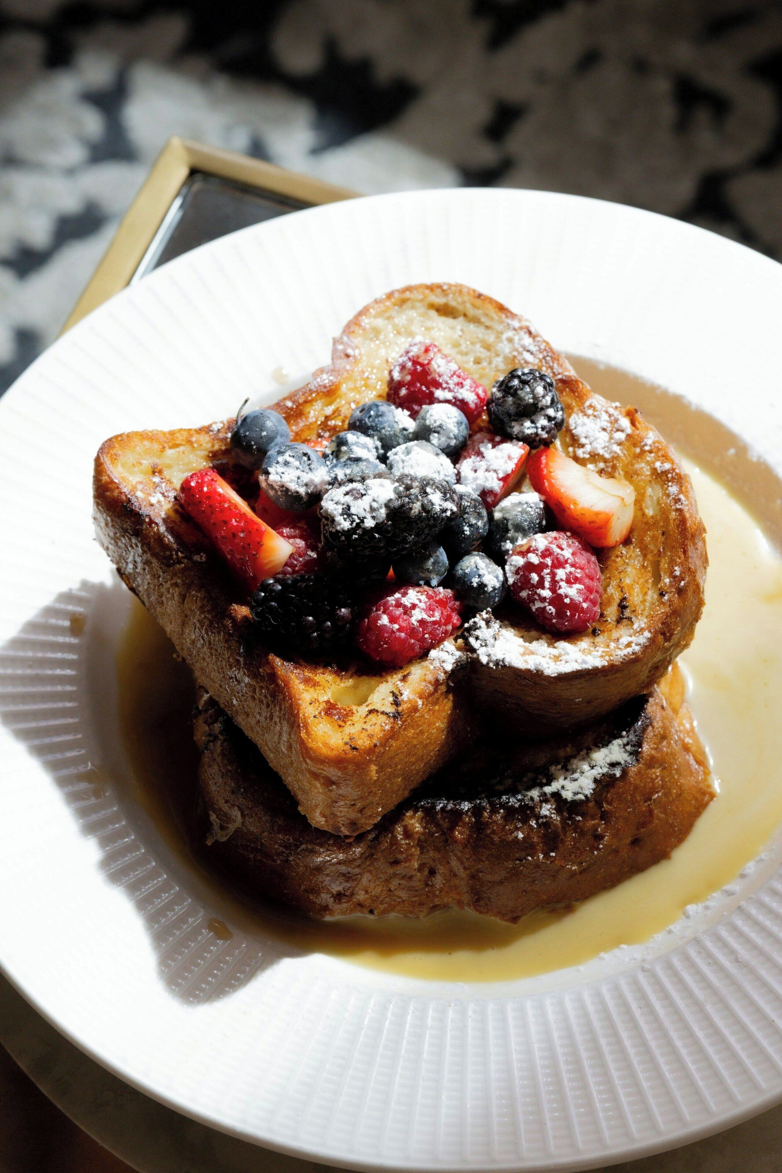 A stack of French toast with berries and powdered sugar on a white plate.