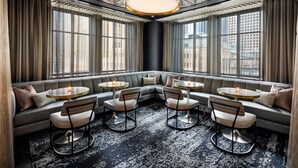 En moderne lounge med buet loft, store vinduer og et siddeområde med runde borde og stole.