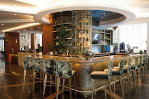 A modern bar area with a curved counter, bar stools, and a decorative plant centerpiece. - Rand Tower Hotel , Minneapolis, A Tribute Portfolio Hotel (Minneapolis)