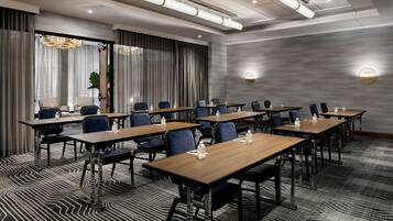 Sala de conferência com várias mesas e cadeiras, carpete estampado e um lustre moderno.