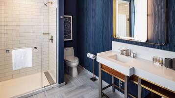Un baño moderno con ducha envuelta en vidrio, un lavamanos blanco con marco dorado y un espejo grande con marco dorado.