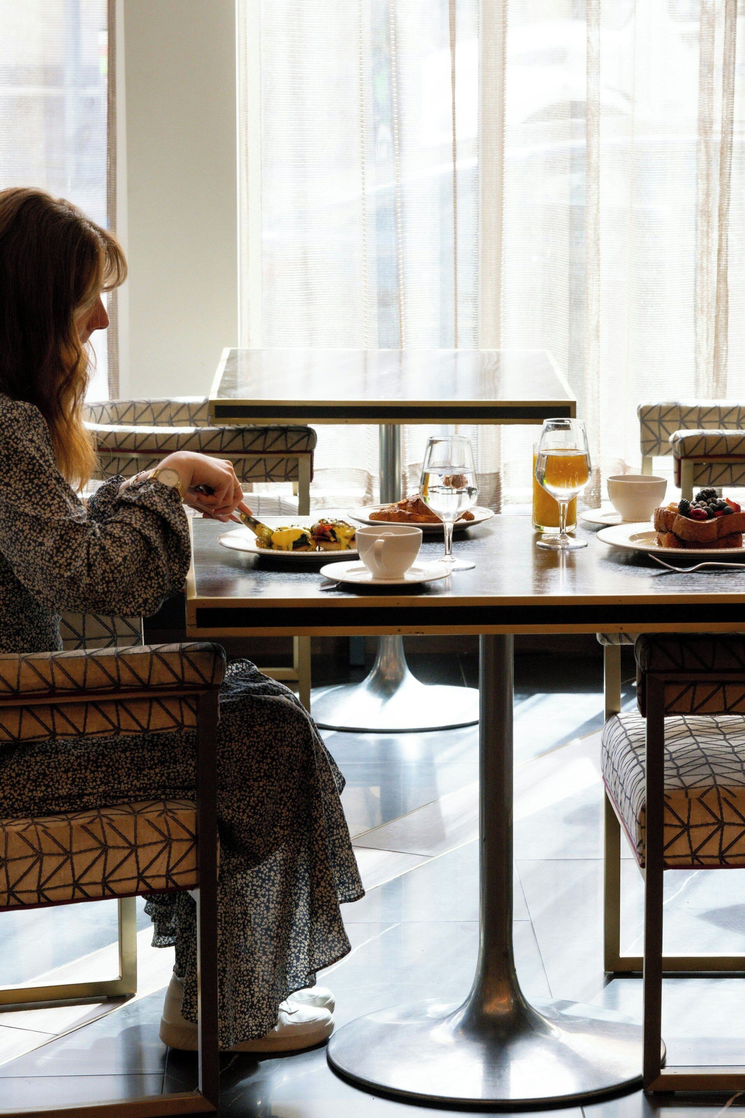 Un comedor con una mesa dispuesta para el desayuno, que incluye bollería, un vaso de zumo de naranja y una taza de café.