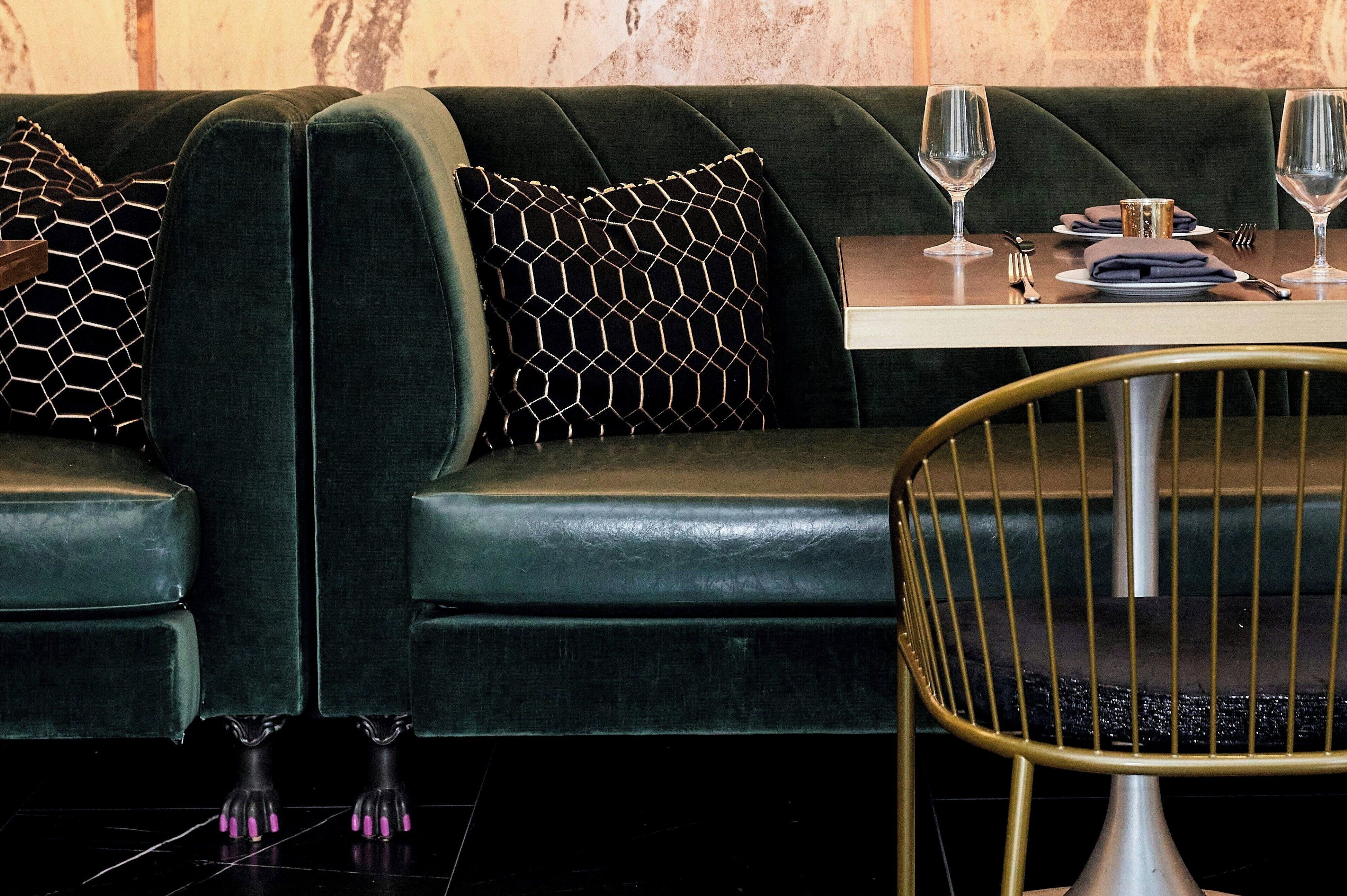 A dark green sofa with a geometric patterned pillow, a small table with a white tablecloth, and a gold chair.