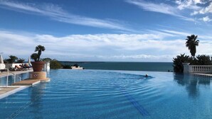 A clear blue infinity pool with a view of the ocean and palm trees. - Sea views and beautiful pool (Cannes)