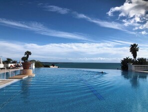 A clear blue infinity pool with a view of the ocean and palm trees.
