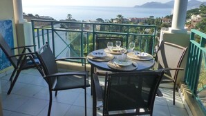 A balcony with a table set for dining, overlooking a scenic view of the sea and distant mountains. - Sea views and beautiful pool (Cannes)