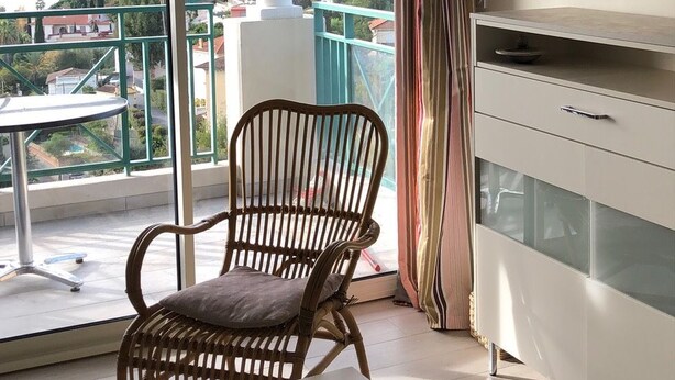A balcony with a view of a body of water and mountains, a wicker chair, a small table, and a cabinet. - Sea views and beautiful pool (Cannes)